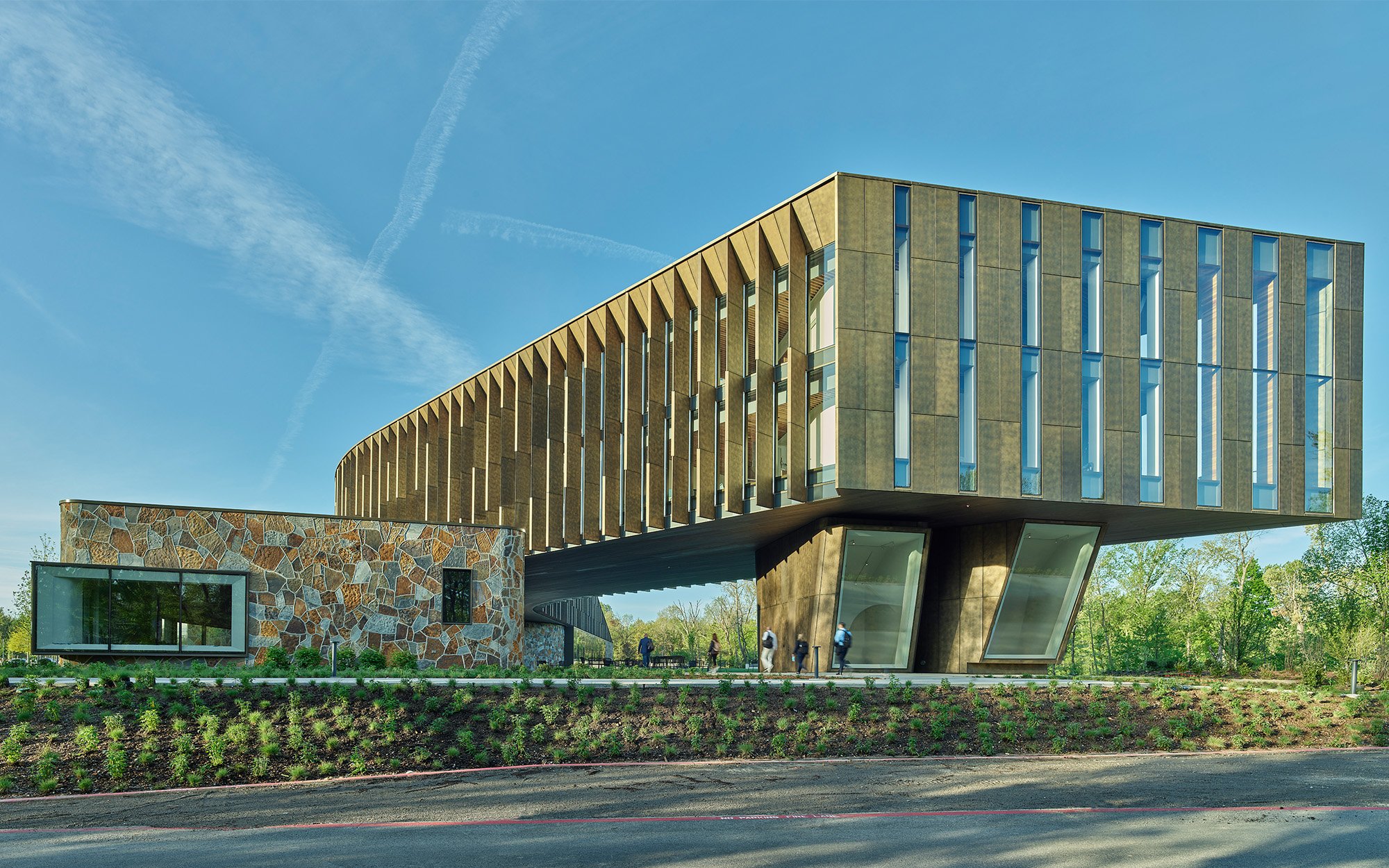 A geometrical building with giraffe stone cladding on the lower box and the elevated building part with a yellowish exterior extended facade.