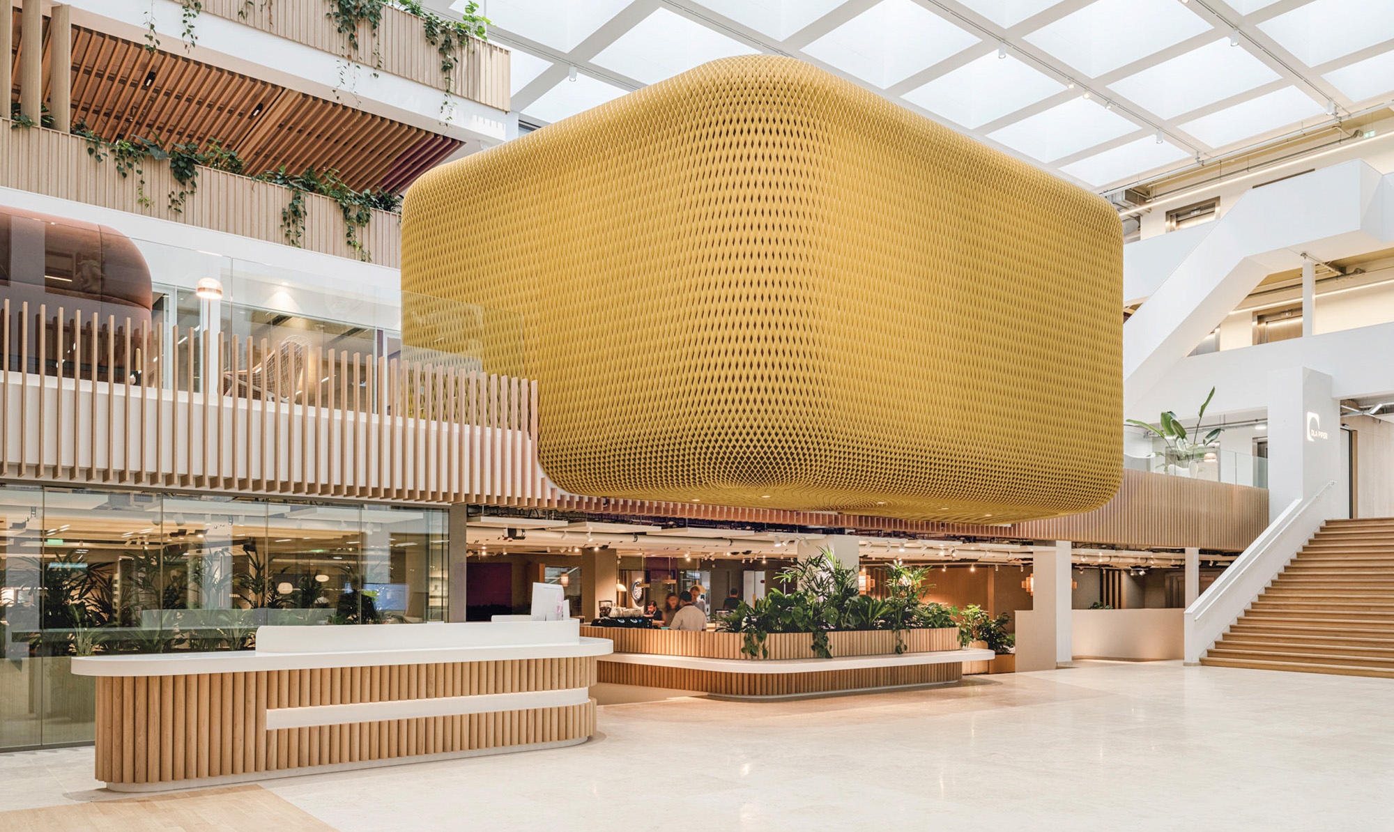 A large yellow 3D printed origami facade like wall structure made from waste material is hanging from the 1st floor of a space.