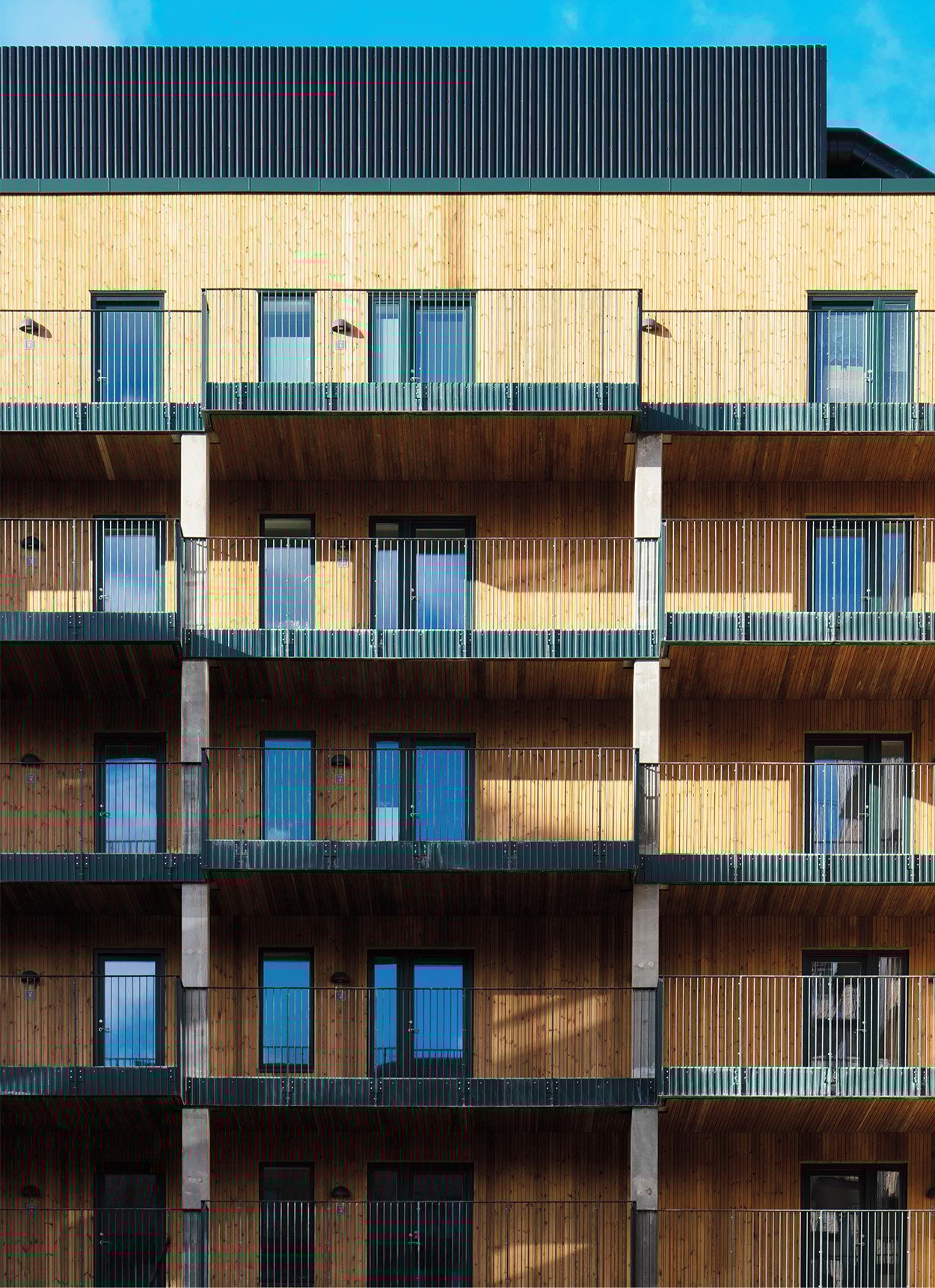 An exterior of a building cladded with bamboo like light material made from waste with multiple equidistant window and doors.