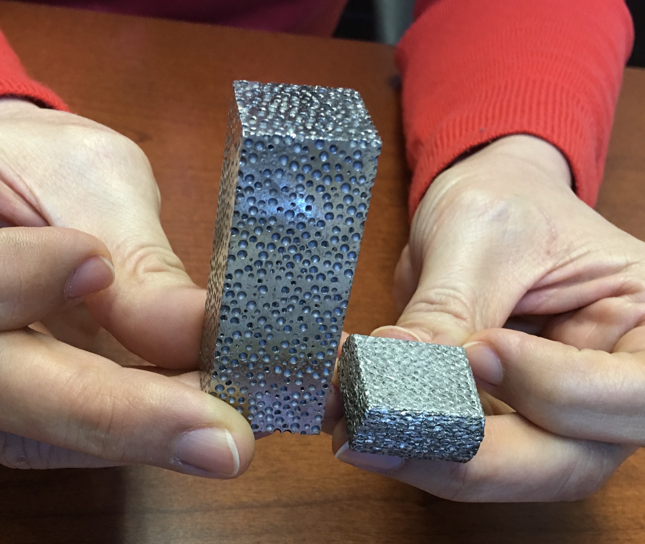Two blocks of composite metal foam in the hands of a woman holding the piece to show how light the weight os this metal block is.
