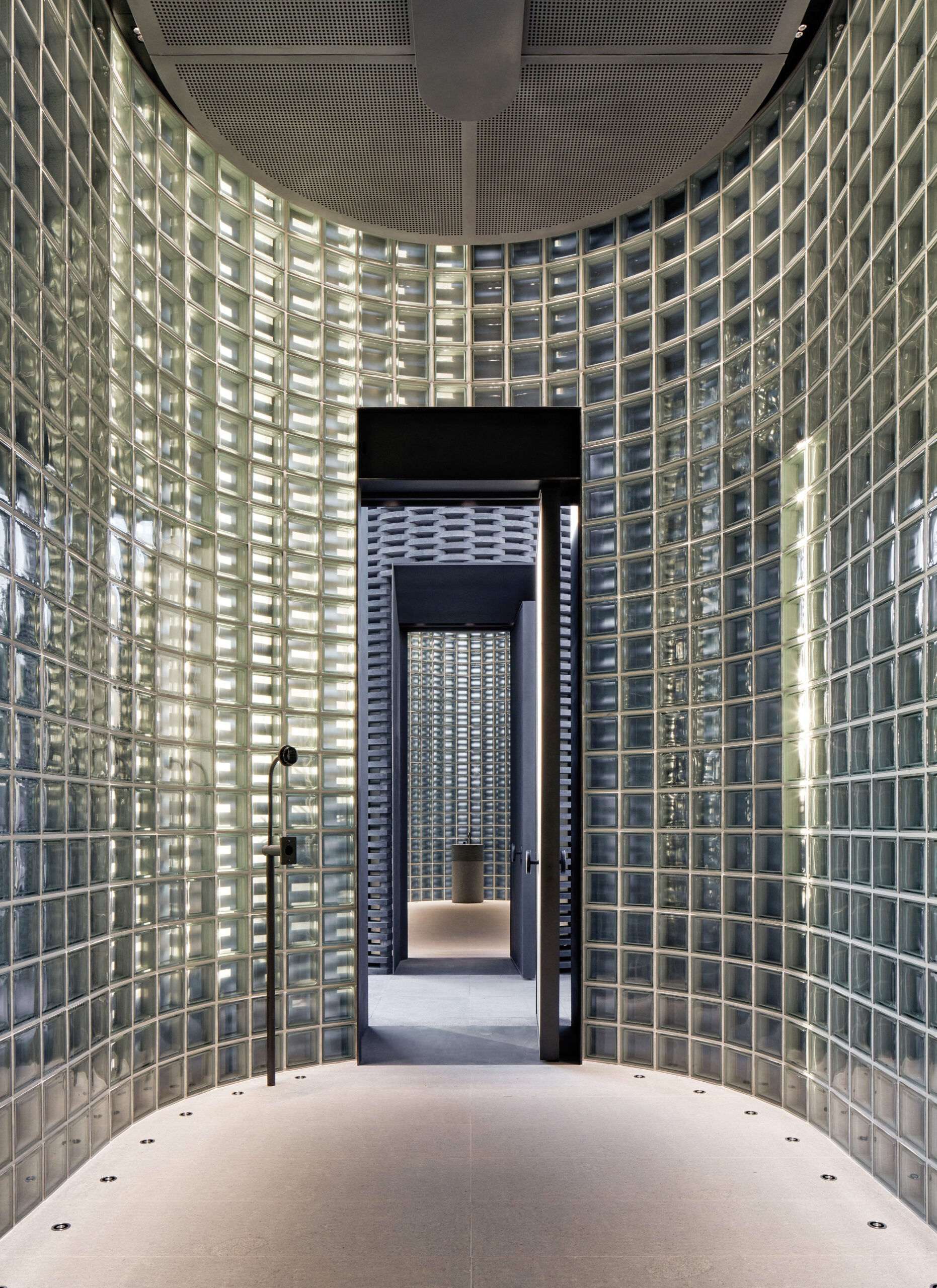 A metal framed glass door opening from a curved wall lined with glass blocks and flushed lights on the floor.