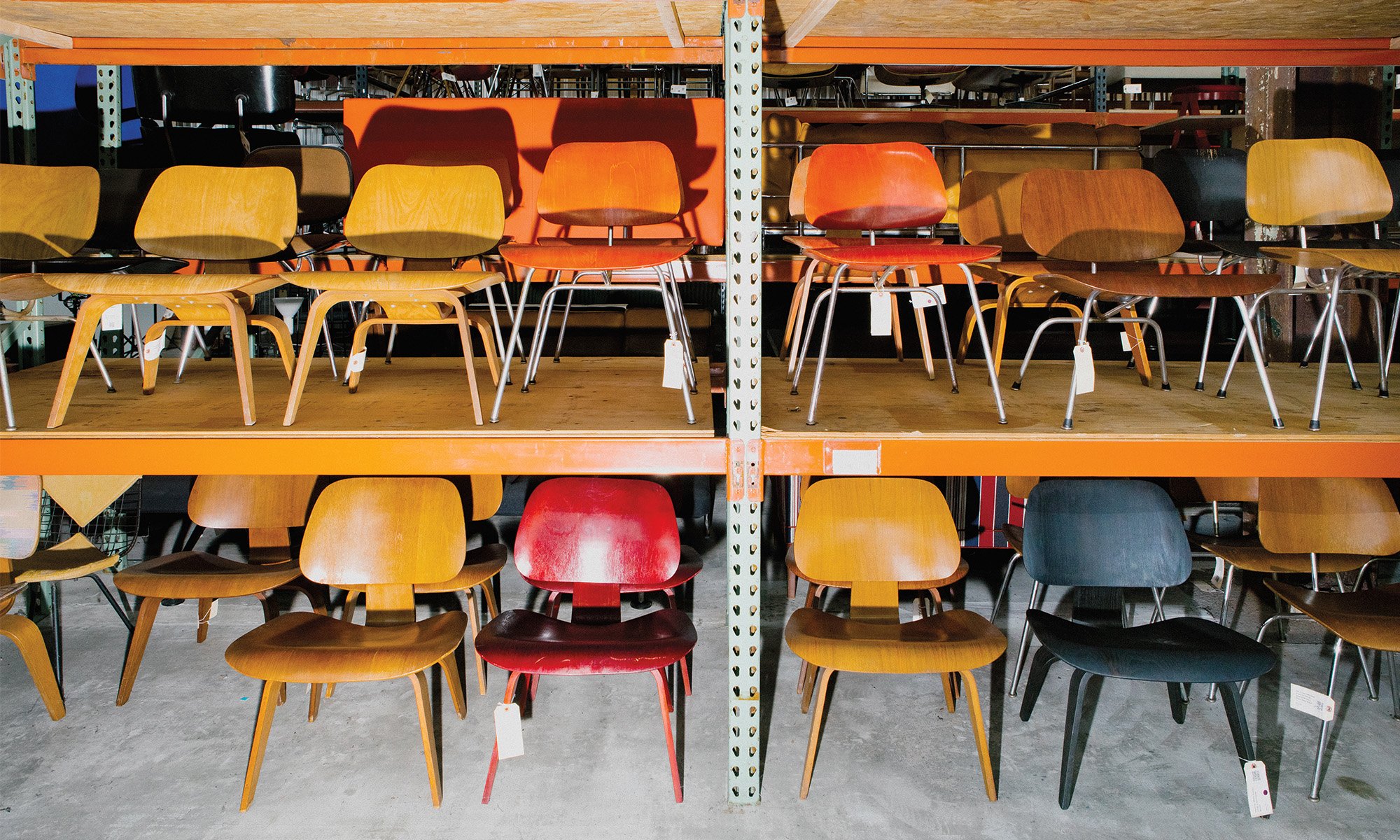 A collection of vintage Charles and Ray Eames wooden chairs in natural stain, red, orange and black kept on rarify's warehouse shelf.