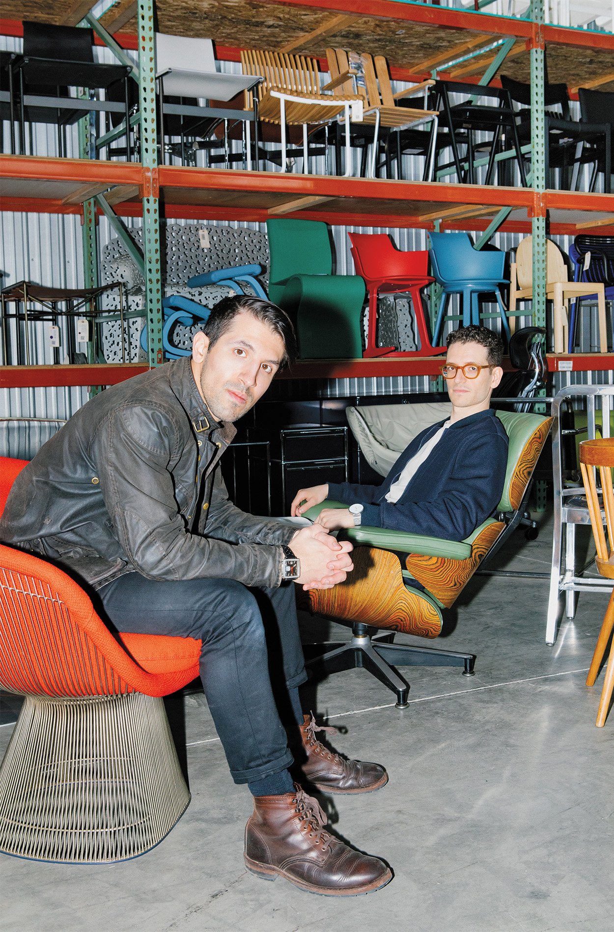 cofounders posing looking at the camera while sitting on their collected furniture in their warehouse location.