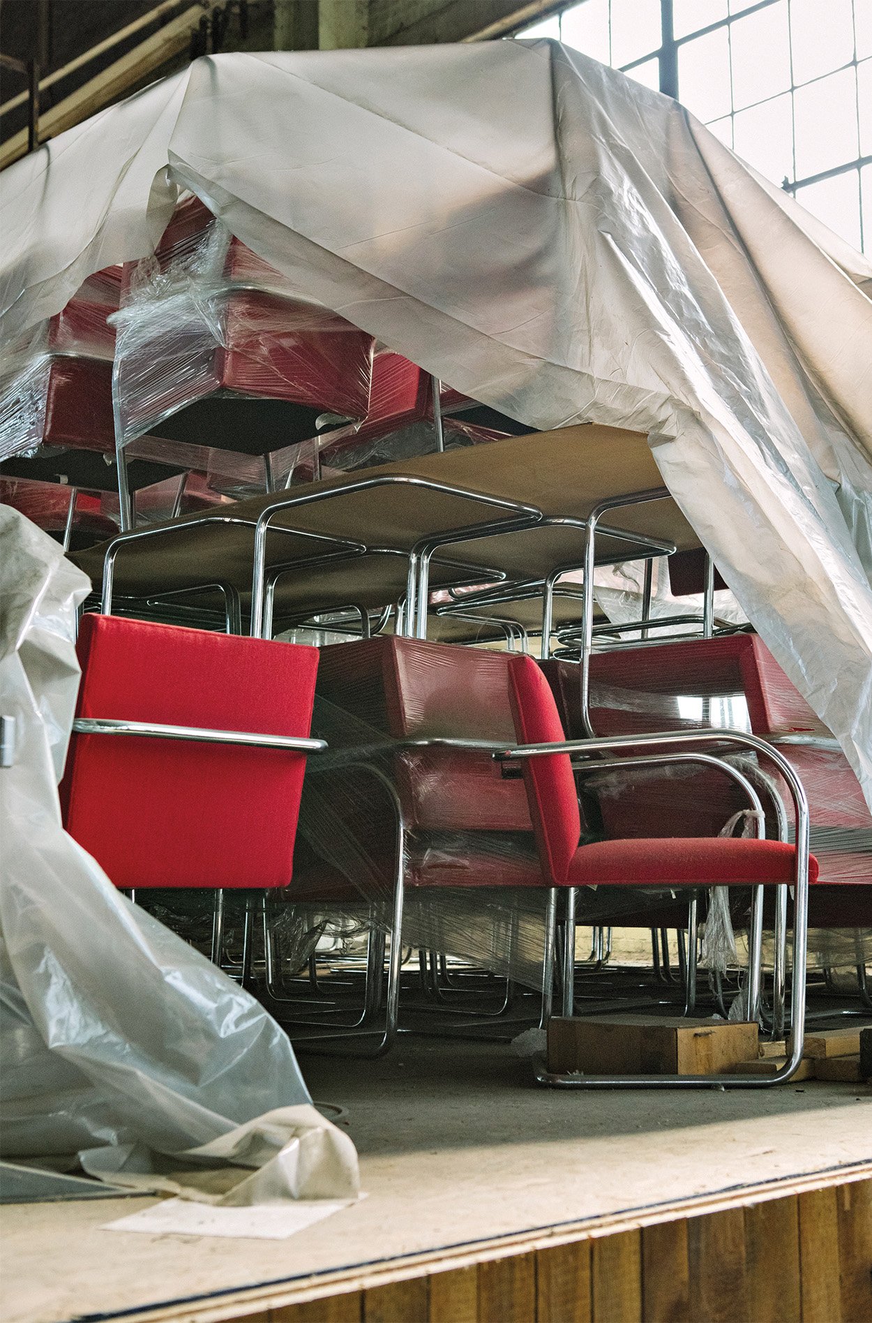 A huge pile of red chairs stacked and covered with tarp and plastic of old Knoll office chairs.