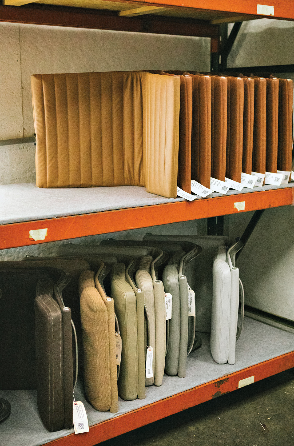 Dismantled seats of the eames chair upholstered in leather and stacked on shelves and arranged by color.