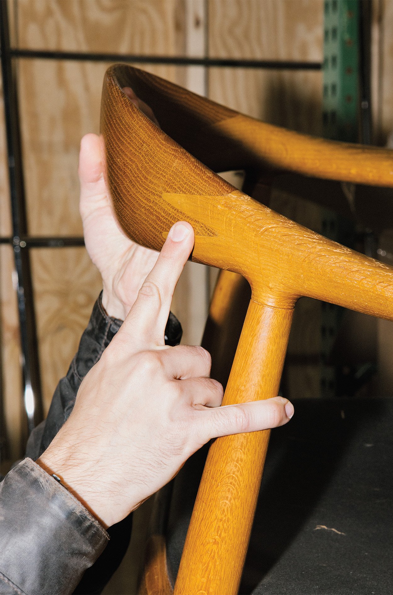 A close shot of a oak wood chair with the founders finger pointing to the detail of the grain.