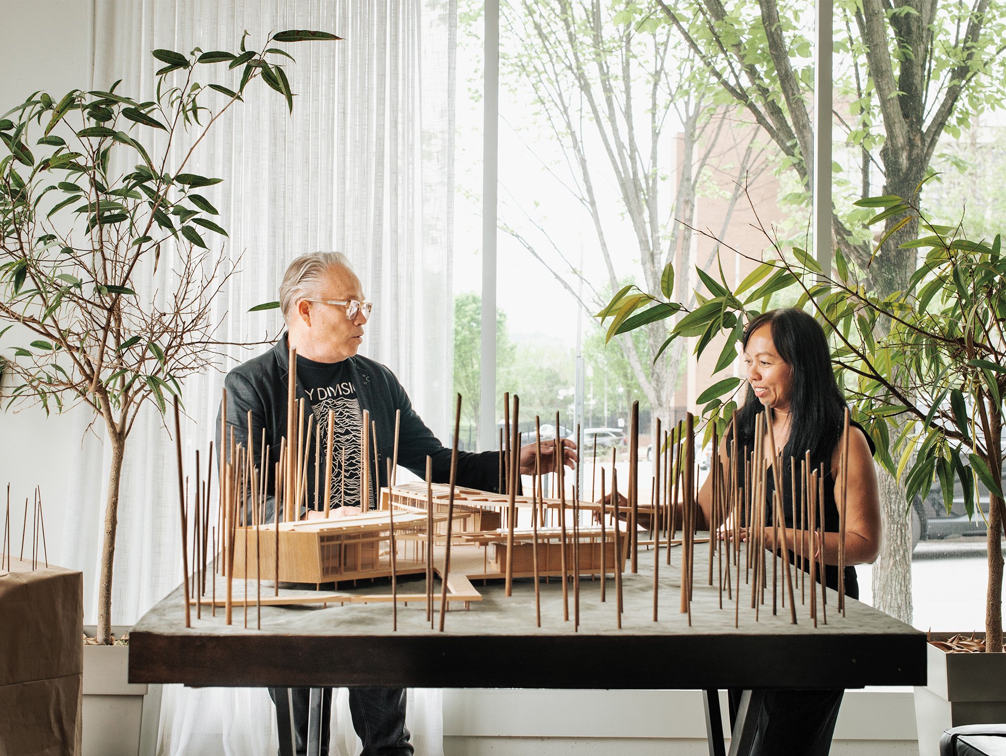 Marlon Blackwell and Ati Blackwell standing behind their sculptural model of the Heartland Whole Health Institute. The 3D model is make completely of miniature wood pieces.