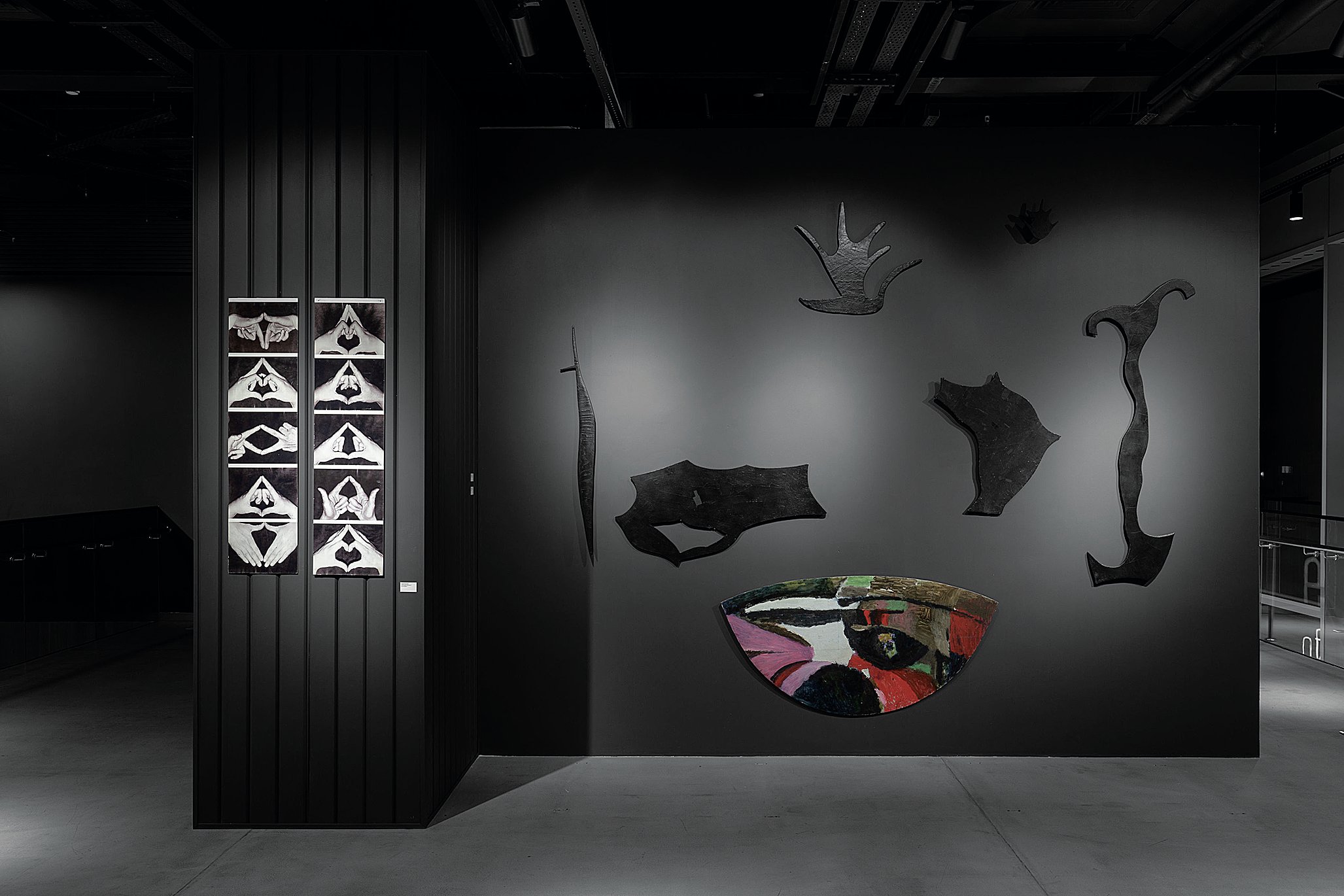 An all black room with studio lights showing 2D pieces of abstract art.