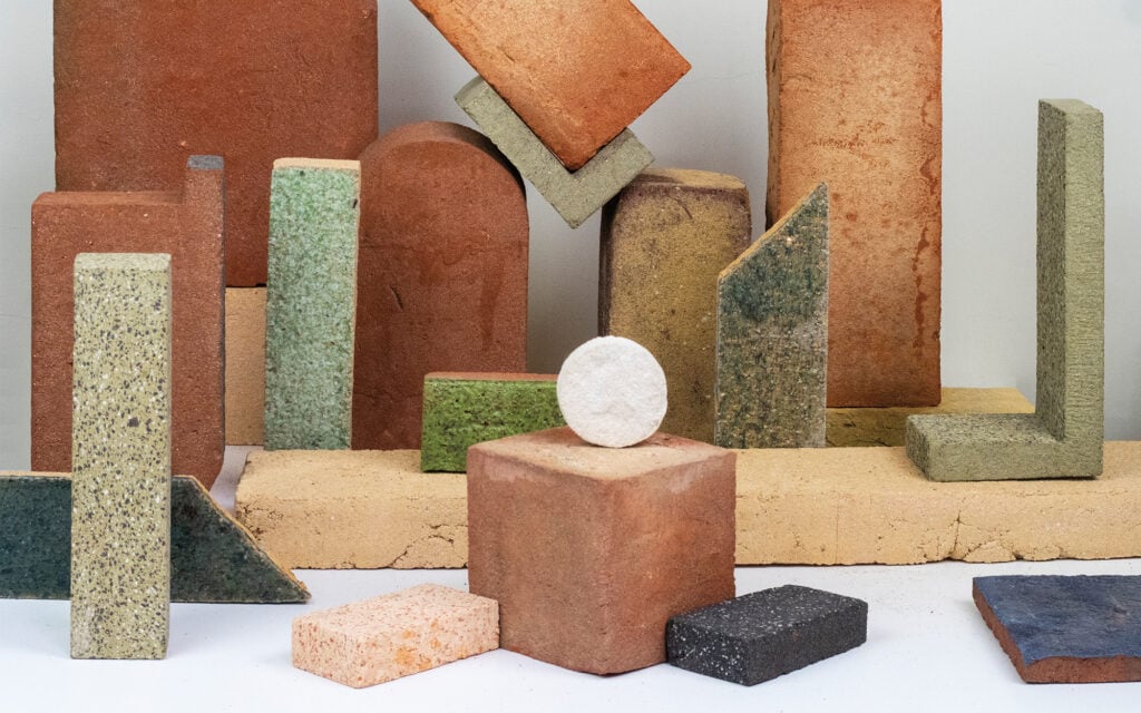 Multiple blocks with curved corners and edged corners in earthy colors made from waste materials and a white ball like structure.