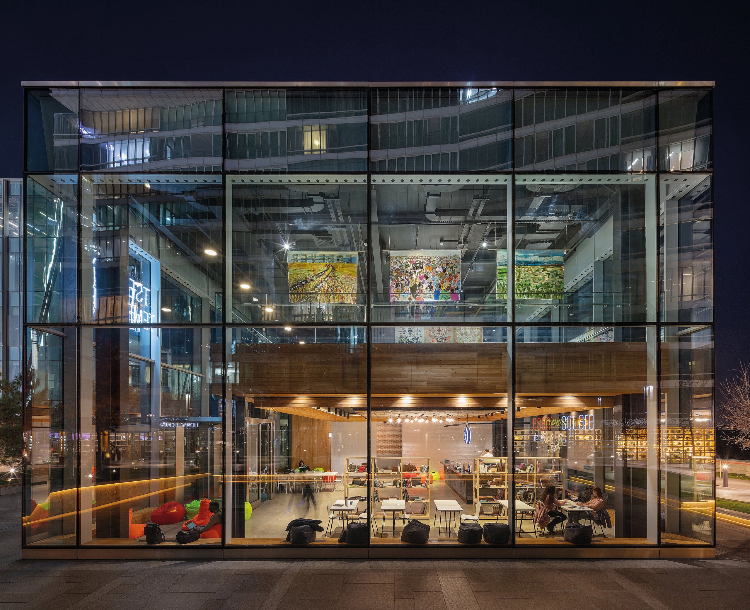 Exterior of an glass building with 2 floors with furniture and art hung from the ceiling.